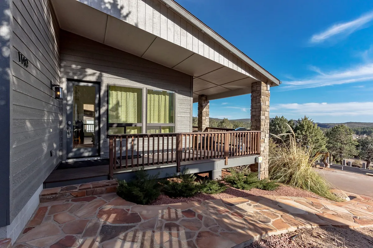 A welcoming porch with wooden railings, green curtains, and stone columns overlooks landscaped pathways. The inviting space is ideal for enjoying morning coffee or evening relaxation, seamlessly blending indoor comfort with outdoor beauty.
