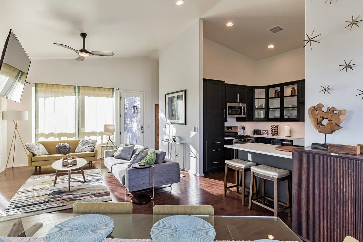 An open living space that seamlessly connects the sofa area, dining table, kitchen, and a window that lets in plenty of natural light. Decorative wall art adds a contemporary touch.
