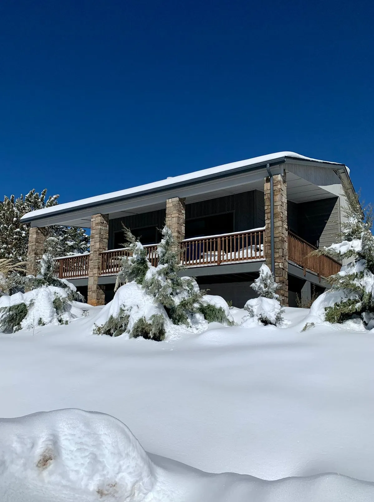 This exterior image depicts a snow-covered front yard, the stone facade of the home, wooden balcony railings, and evergreen trees. The well-maintained exterior and visible parking area communicate a sense of security and easy arrival, echoing the section's focus on seamless check-in and off-street parking.