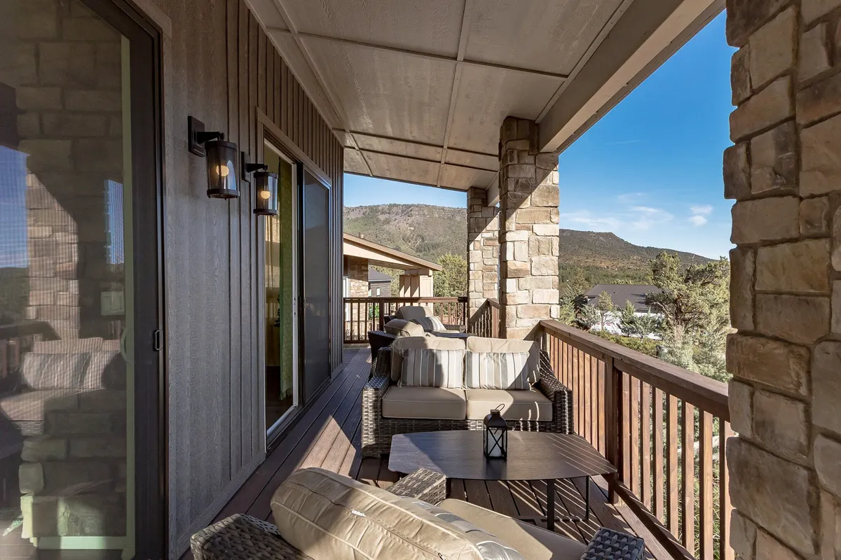 A cozy seating arrangement on a wooden deck is framed by a rustic railing, with lanterns on the table and a panoramic mountain view stretching into the distance. The setting sun casts a tranquil glow, emphasizing the peaceful, private ambiance of the deck and its suitability for both relaxation and entertaining guests.