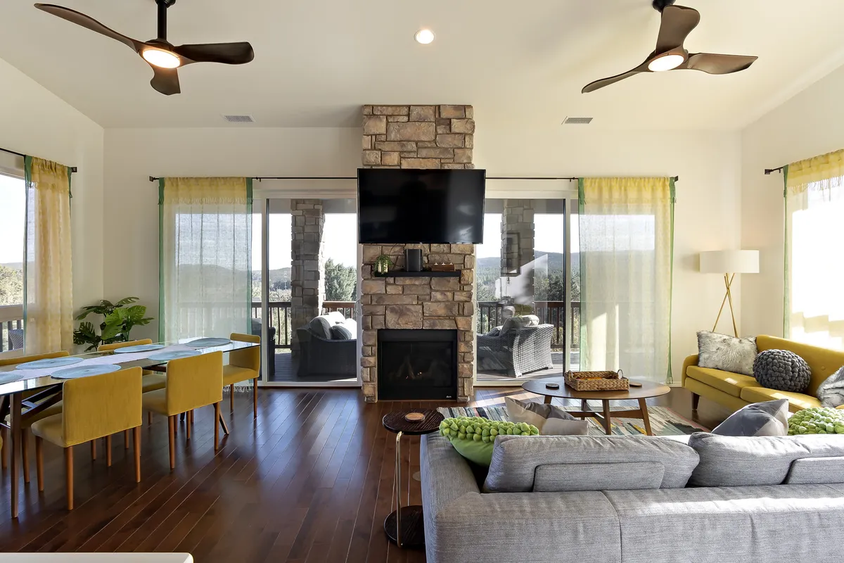 An inviting interior living space featuring a stone fireplace, large windows with scenic views, a dining area, and a comfortable seating arrangement. The room is bright and welcoming, suggesting both relaxation and hotel-style comforts.