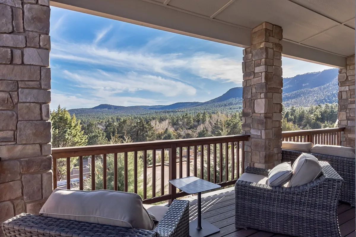 A serene outdoor seating area overlooking a lush, green mountain range. The deck offers a comfortable place to relax and enjoy sweeping panoramic views, with plenty of space for a couple to savor a coffee at sunrise or stargaze at night. The sky appears expansive, lending itself perfectly to tranquil mornings or romantic evenings.
