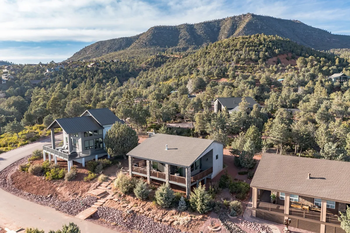A serene exterior shot of modern homes nestled among lush greenery, with a majestic mountain backdrop. The porches and trails invite guests to step outside and enjoy sunrise views, nature walks, and stargazing sessions in the tranquil setting.
