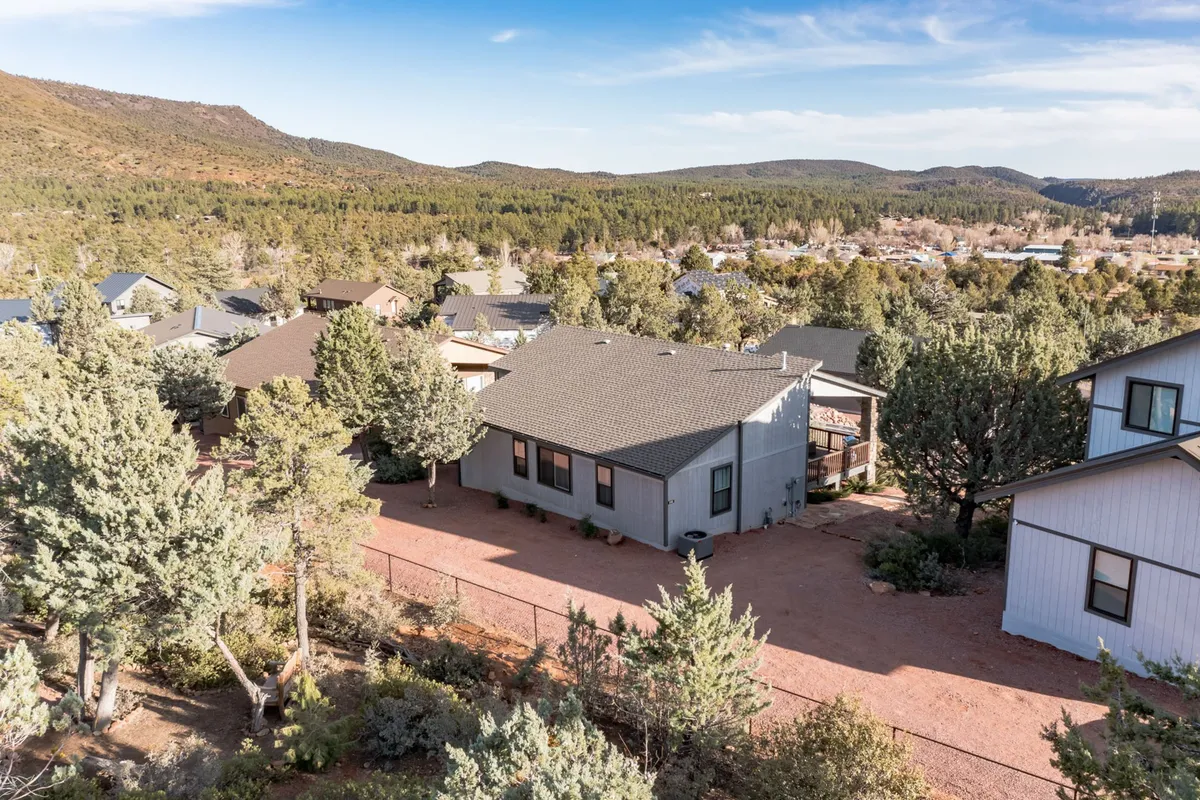 This image displays the house nestled among tall trees with a picturesque mountain range in the background. The landscaping highlights a sense of place, while the peaceful scene evokes small-town tranquility and easy access to nature.