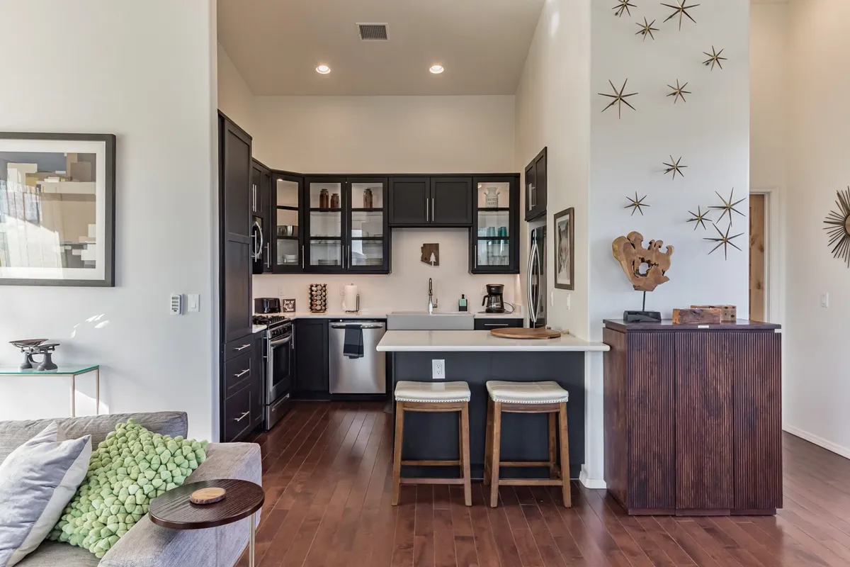 A modern kitchen with sleek appliances, artistic wall decor, and a breakfast bar with stools. The space is designed for cooking and entertaining, flowing openly into the living area.